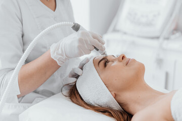 A beautician uses a vacuum machine to cleanse the client's face in a beauty salon, providing...