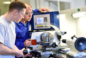 young apprentices in technical vocational training are taught by older trainers on a cnc lathes machine - 728676985