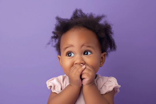 Scared African American baby girl and biting nails in studio with oops reaction on purple background.