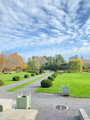 Park in autumn. Paved driveway with shrubs on both sides leading to a water fountain. Structured...