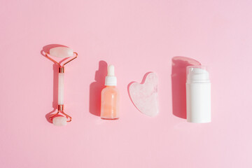 Obraz na płótnie Canvas Cosmetic cream and serum bottles, facial roller and gua sha stone on pink background with shadows. Skin care concept. Top view, flat lay