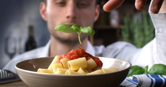 Super slow motion of a professional chef is putting on  fresh green basil leaf on traditional Italian dish of pasta penne with red tomato sauce in restaurant kitchen at 1000 fps.
