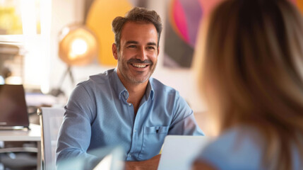 man is smiling at a woman across a table with a laptop in the foreground