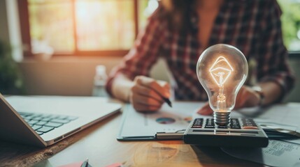 Conceptual image of a person holding a glowing light bulb with a calculator and paperwork on a desk, symbolizing idea generation and financial planning.