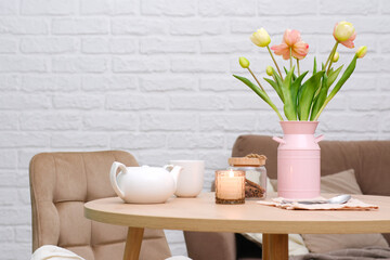 Home spring interior in living room. Pink vase with tulip,hot teapot, burning candle, cup of tea on...
