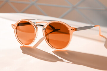 Elegant peach fuzz sunglasses with transparent sepia lenses on minimal light background. Modern...