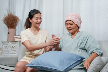 Obraz premium Daughter lovingly hands glass of milk to mother. By taking care during cancer treatment. daughter runs house has to keep her mother, wears warm beanie, at home. Received care while battling cancer