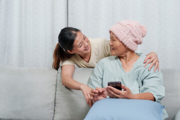 Daughter leans in with concern as her mother, in pink cap, navigates her phone, moment of connection. comforting scene of a young woman attentively watching her mother using smartphone, in cozy home
