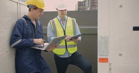 Two engineers construction workers are intently analyzing data discussing project details on their tablets at the job site cityscape rooftop of city building