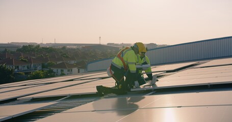Two engineers solar technicians in reflective gear discussing working examine solar installations on rooftop panels at dusk, with suburban backdrop
