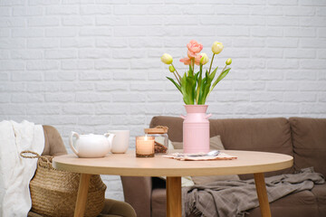 Home spring interior in living room. Pink vase with tulip,hot teapot, burning candle, cup of tea on...