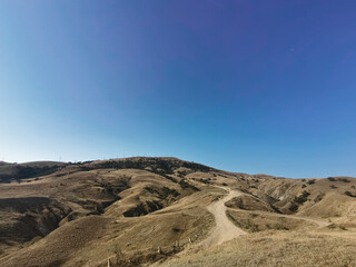 Photograph of Sandy Hills and Winding Dirt Road Under a Blue Sky, Sunny Day