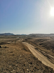 Photograph of Sandy Hills and Winding Dirt Road Under a Blue Sky, Sunny Day