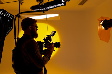 Back angle view of high definition digital video camera which recording or shooting tv commercial production on pan tilt shift professional head tripod at outdoor location and film crew team with set.