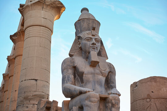 Seated statue of Ramesses II by the First pylon of the Luxor Temple, Egypt. Columns and statues of the Luxor temple main entrance, first pylon, Egypt