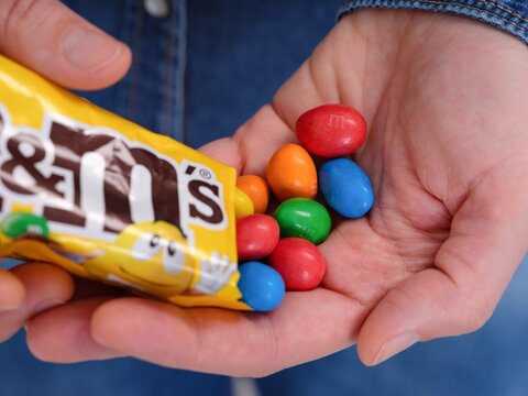 Tambov, Russian Federation - January 23, 2024 A woman pouring M&Ms in to her hand from a packet.