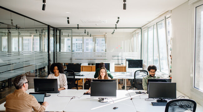 In a spacious and bright office, a diverse team is focused on individual tasks at their workstations, epitomizing the concept of independent productivity within a shared, supportive co-working space