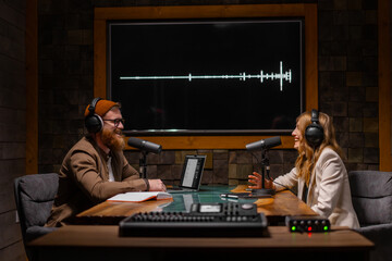 Two radio hosts talking and smiling while sitting near microphones in broadcasting studio
