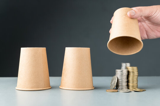 Closeup hand of a man that choose the one of cups in three cups shell game and found the right one that has a lot of money, investment, and chance