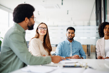 A diverse team listens attentively, with a male employee making a point, which reflects an engaged brainstorming session and a culture of open communication. Concept of a focused working atmosphere
