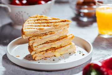 Toast sandwich with gouda cheese and turkey ham  on a bright background with ingredients in blurry background. Served with orange juice  and eggs