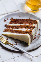 A piece of carrot cake served on rustic plate placed on bright sunny scene. Layered cake with cream cheese frosting and fluffy biscuit. Served with tea. 