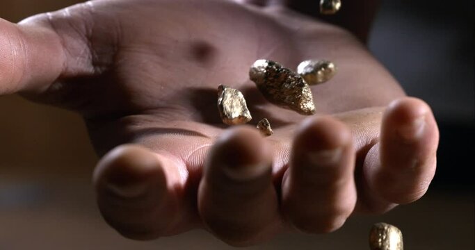 Super slow motion macro of precious raw metal rocks gold nuggets are falling on workers hand for quality control at 1000 fps.