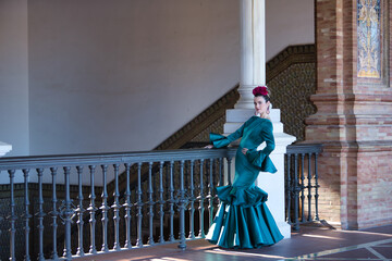 Young, beautiful, blonde woman in typical green colored flamenco suit, posing next to a wrought...