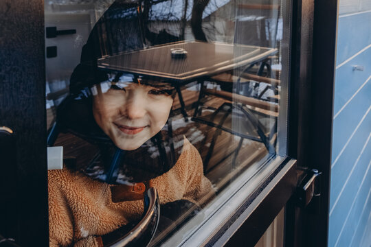  Portrait Of A Child Looking Through A Window Or Glass Door Decorated With Christmas Decorations To The Street