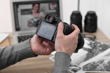Professional photographer with digital camera at wooden table indoors, closeup
