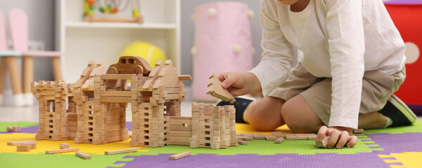 Little boy playing with wooden construction set on puzzle mat in room, closeup. Child's toy