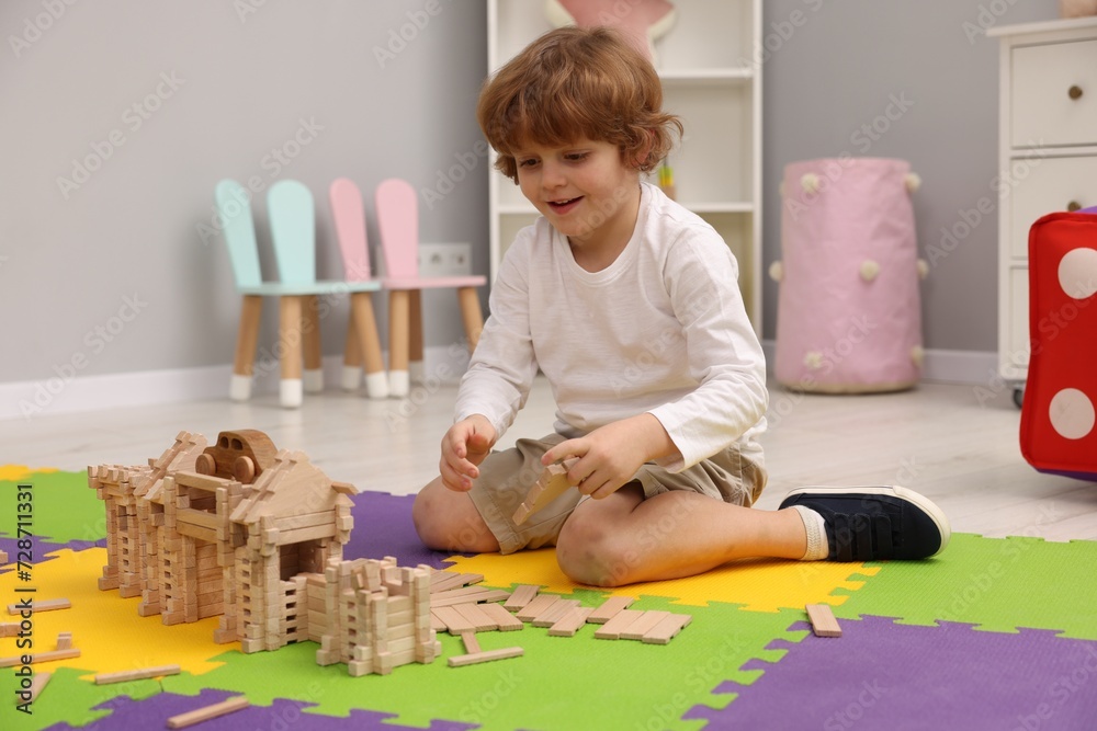 Poster Little boy playing with wooden construction set on puzzle mat in room. Child's toy