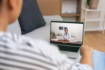 Patient at home in a relaxed setting engaging with a doctor on a laptop, representing the...