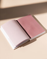 Open trendy journal on tan background with sunlight and shadows with blank pages