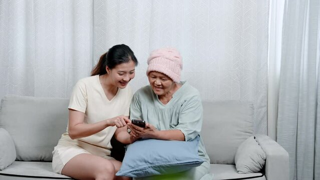 Asian mother suffering from cancer cute daughter, looking at mobile phone together, watching funny clips on phone causes laughter while looking at cell phone, free time activities that do together.