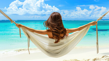 A woman with loose hair in a hammock attached to palm trees enjoys relaxing on a sandy beach against the backdrop of blue sea waves. Holidays on a paradise island.