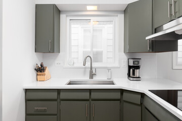 A kitchen detail with green cabinets, white countertop, and a subway tile backsplash.