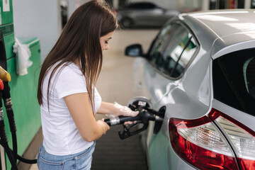 Fototapeta na wymiar Attractive young woman refueling car at gas station. Female filling diesel at gasoline fuel in car using a fuel nozzle. Petrol concept. Side view