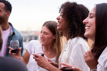 Multiethnic group of friends having fun in a terrace, laughing, talking, and drinking red wine....