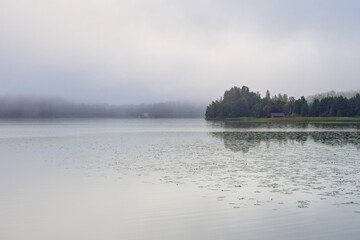 Morning fog on Tuusula Lake in Finland, forest and small house in early September.