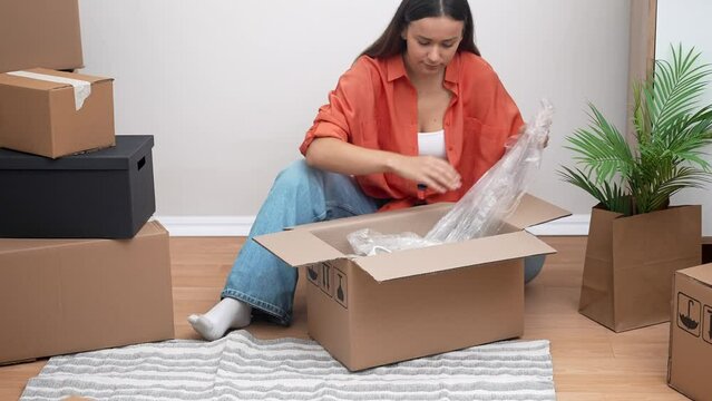 A young woman radiates happiness as she unboxes in her new rented home, embracing the joys of relocation and a fresh start