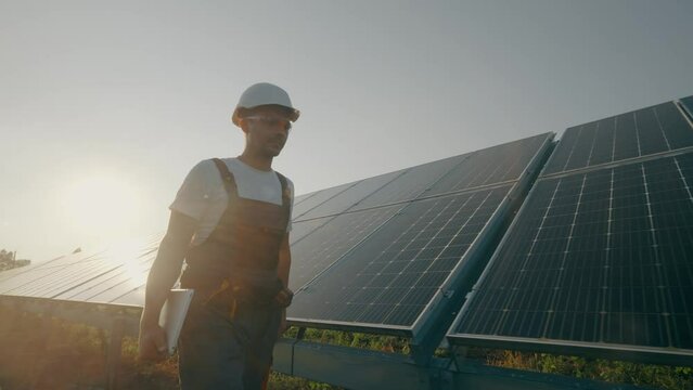 A male engineer with technical documentation walks between solar panels