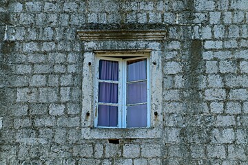 Old wooden window on a stone wall with light pink curtains

