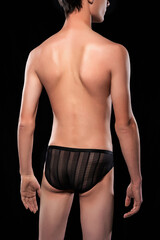 Close-up shot of a young man in black fishnet briefs. Portrait of a male model with no face wearing erotic underpants standing on a black background. Back view.