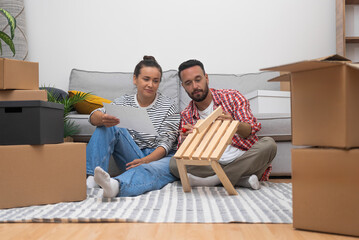 Woman joins in assembling furniture with husband sitting on floor among boxes with other wooden...