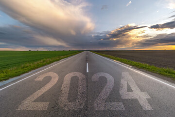 inscription 2023, 2024 and start on asphalt road highway with sunrise or sunset sky background. ...