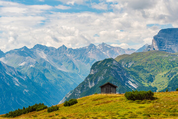 A small wooden hut perched on a green hill high in the mountains, picturesque alpine landscape in...