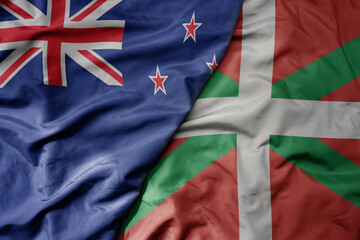 big waving national colorful flag of basque country and national flag of new zealand .