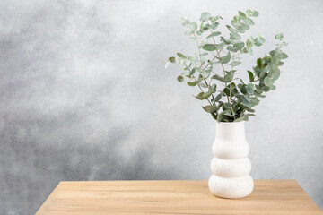Fototapeta na wymiar Green eucalyptus leaves in a vase stand on a chest of drawers against the background of a wall. Aromatherapy.Beautiful eucalyptus bouquet.Minimalist interior with flowers, candles and aroma diffuser.