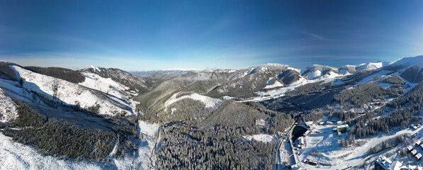 Aerial winter view of Demanovska Dolina village in Low Tatras mountains, Slovakia. Drone panoramic view to countryside landscape, high peaks and tops of frozen fir trees, houses and road of town © Flash Vector